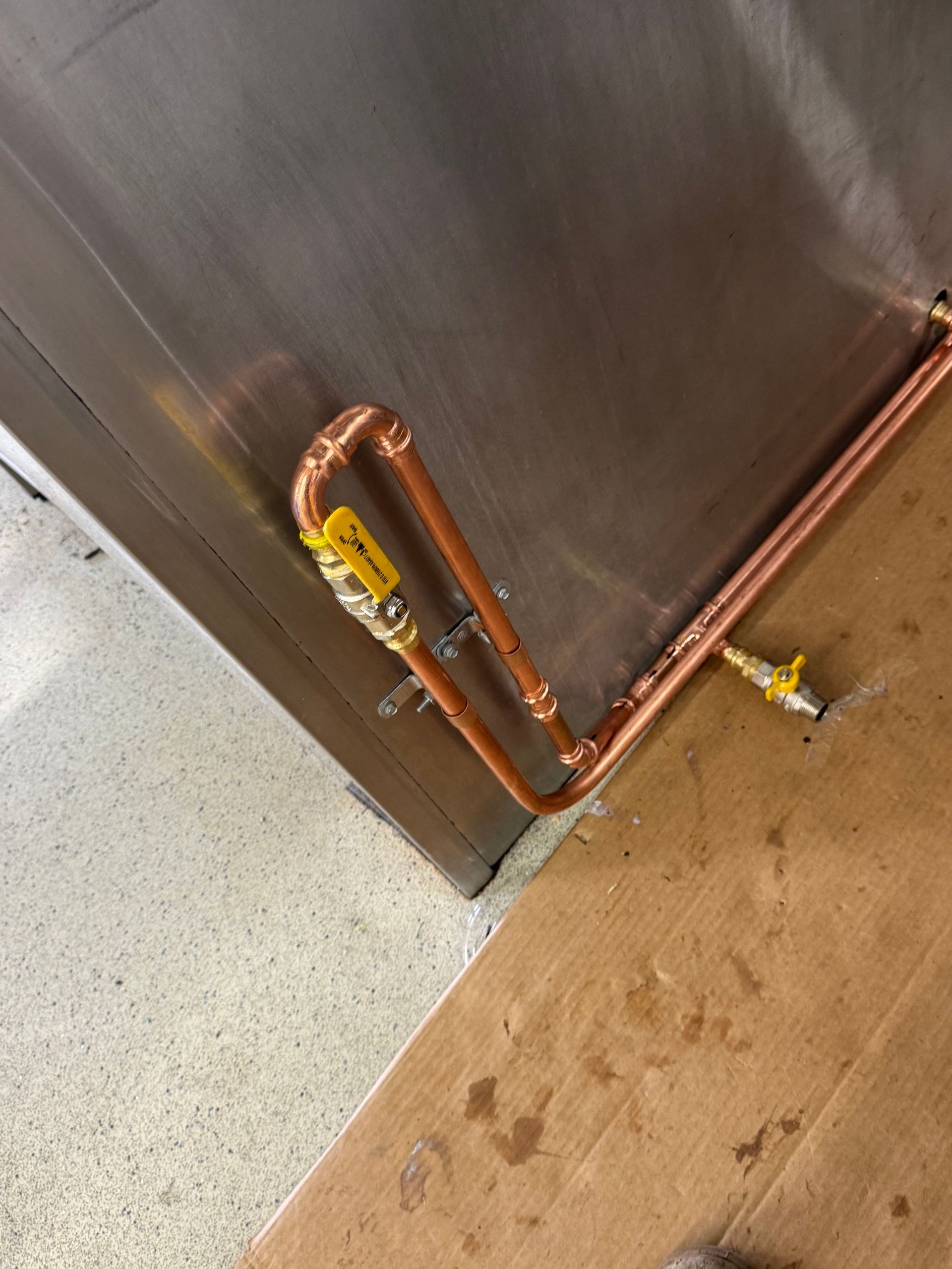 Copper pipes with yellow valves are attached to a stainless steel wall and floor  — Fair Plumbing In Shellharbour, NSW