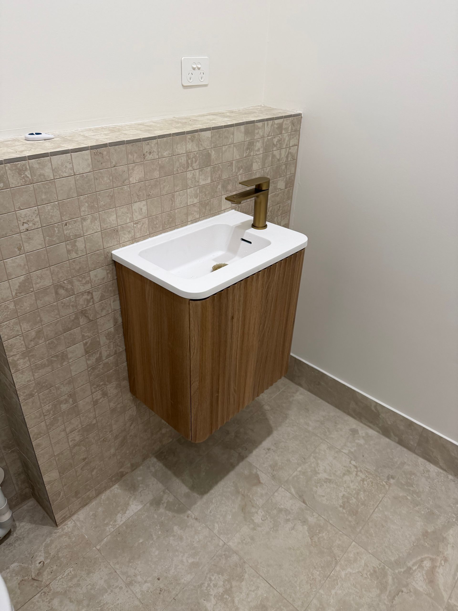 Floating wooden vanity with white sink and gold faucet against textured wall — Fair Plumbing In Shellharbour, NSW