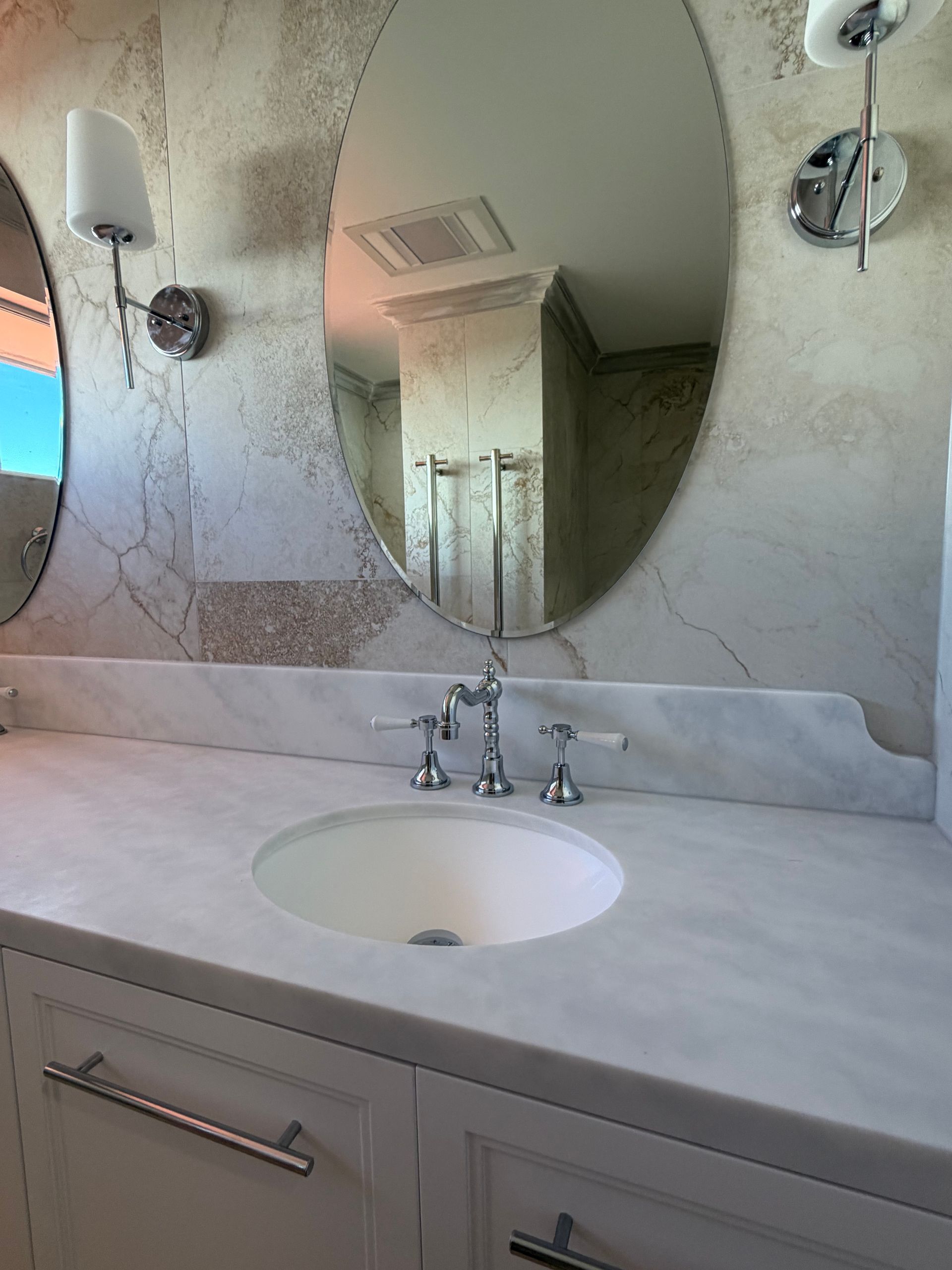 Bathroom vanity with oval mirror, white countertop, sink, chrome faucet, and sconces  — Fair Plumbing In Shellharbour, NSW