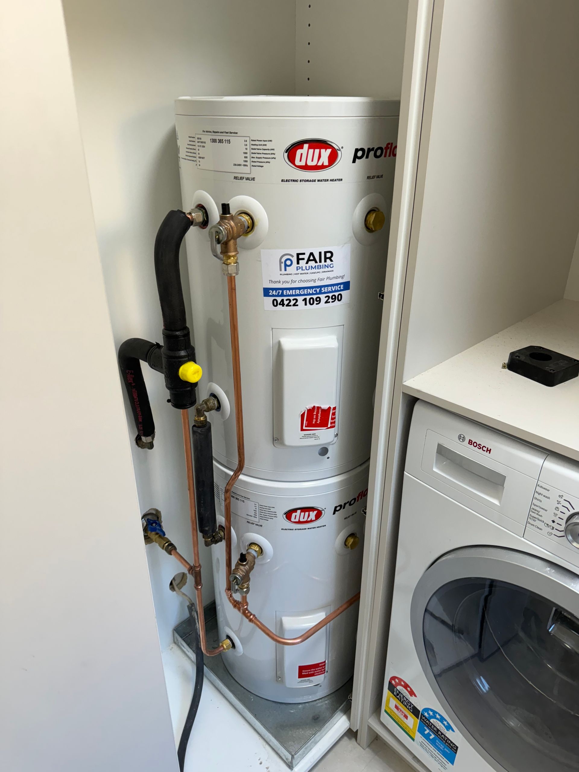 White hot water heater in a laundry closet next to a washing machine  — Fair Plumbing In Shellharbour, NSW