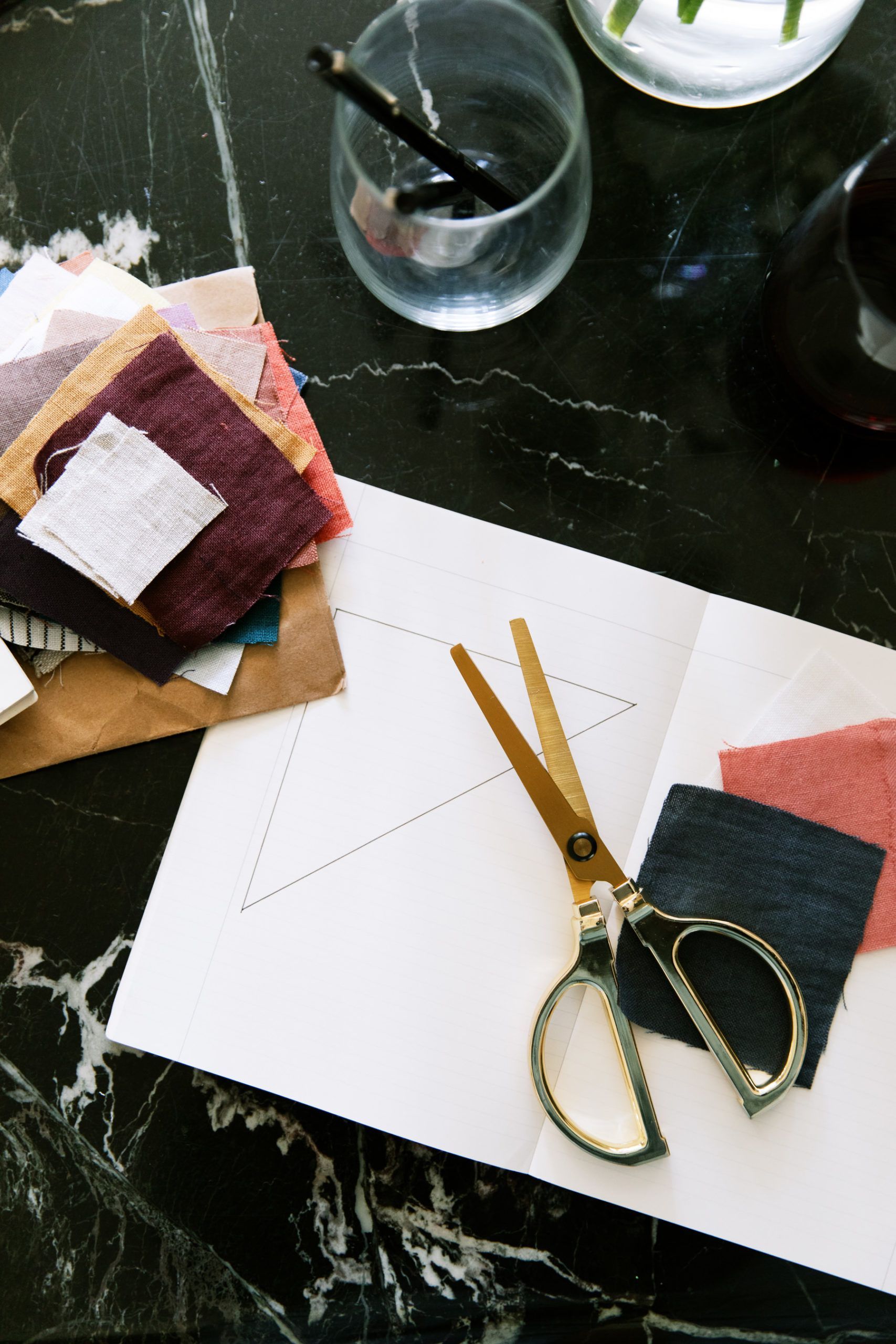 an open notebook with gold luxurious scissors laying on top of deep fabrics with a glass of water