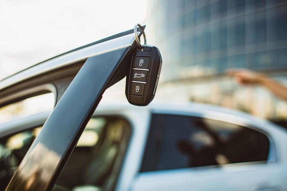 Car key hanging from an open car door. Modern building in the background.
