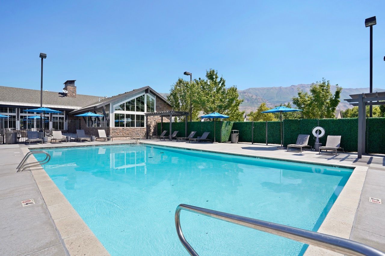 Outdoor pool at a multifamily community with blue water, lounge chairs, and blue umbrellas at Viewpointe—offering apartments for rent in Pleasant Grove, UT.