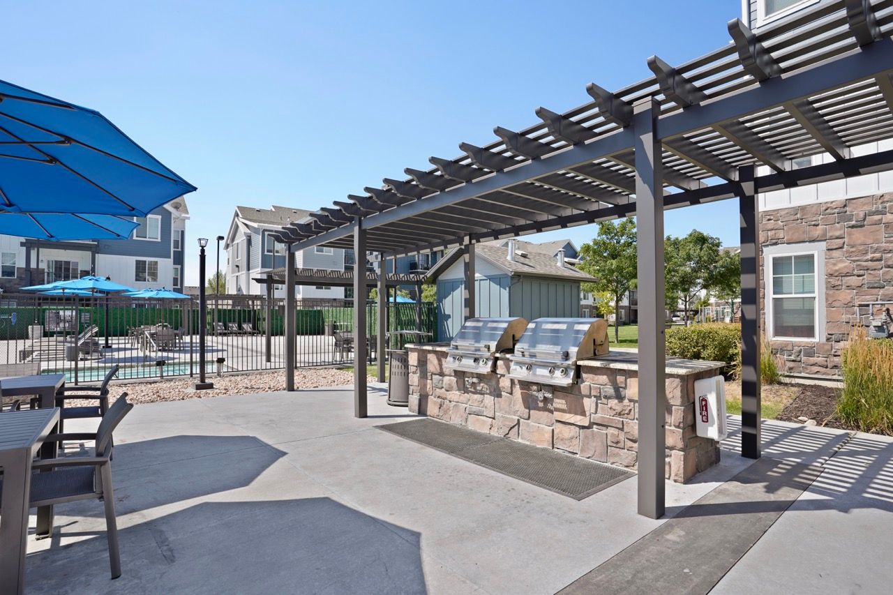 Outdoor community grilling area with stone counters under a pergola, pool and seating in background at Viewpointe—offering apartments for rent near Salt Lake City.