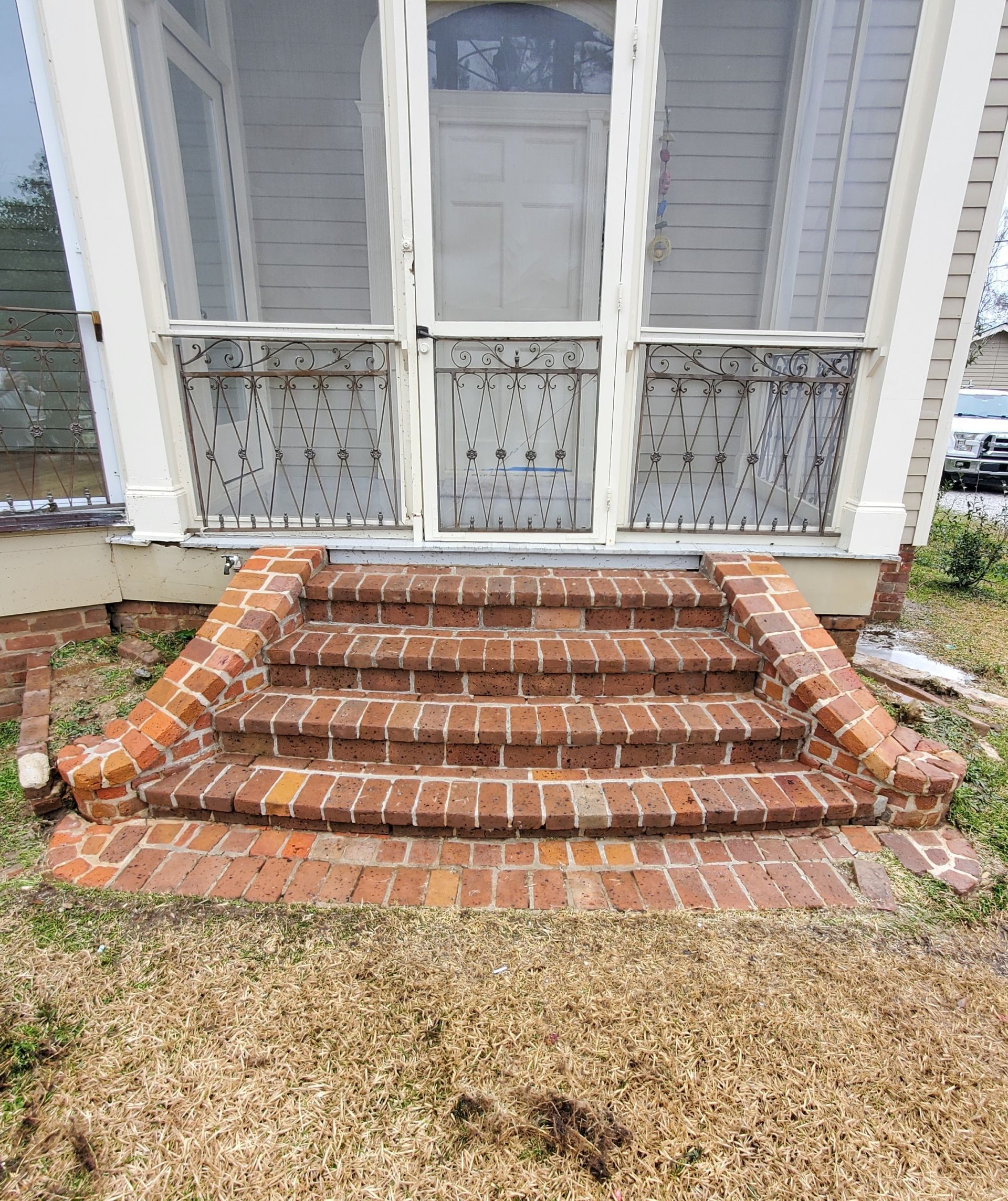 Three wide, reddish-brown brick steps lead to a screened-in porch with a central white door.
