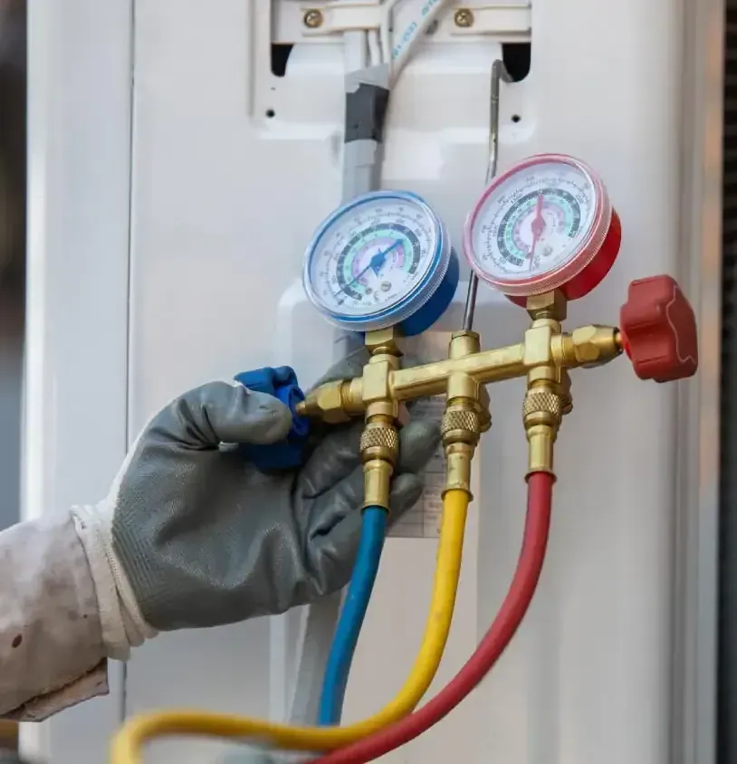 A person in gloves adjusting gauges on an air conditioning unit with blue, red, and yellow hoses.