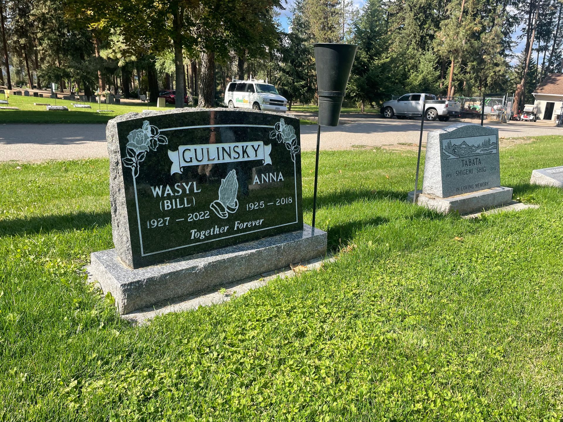 A gravestone in a cemetery with a vase in the background.