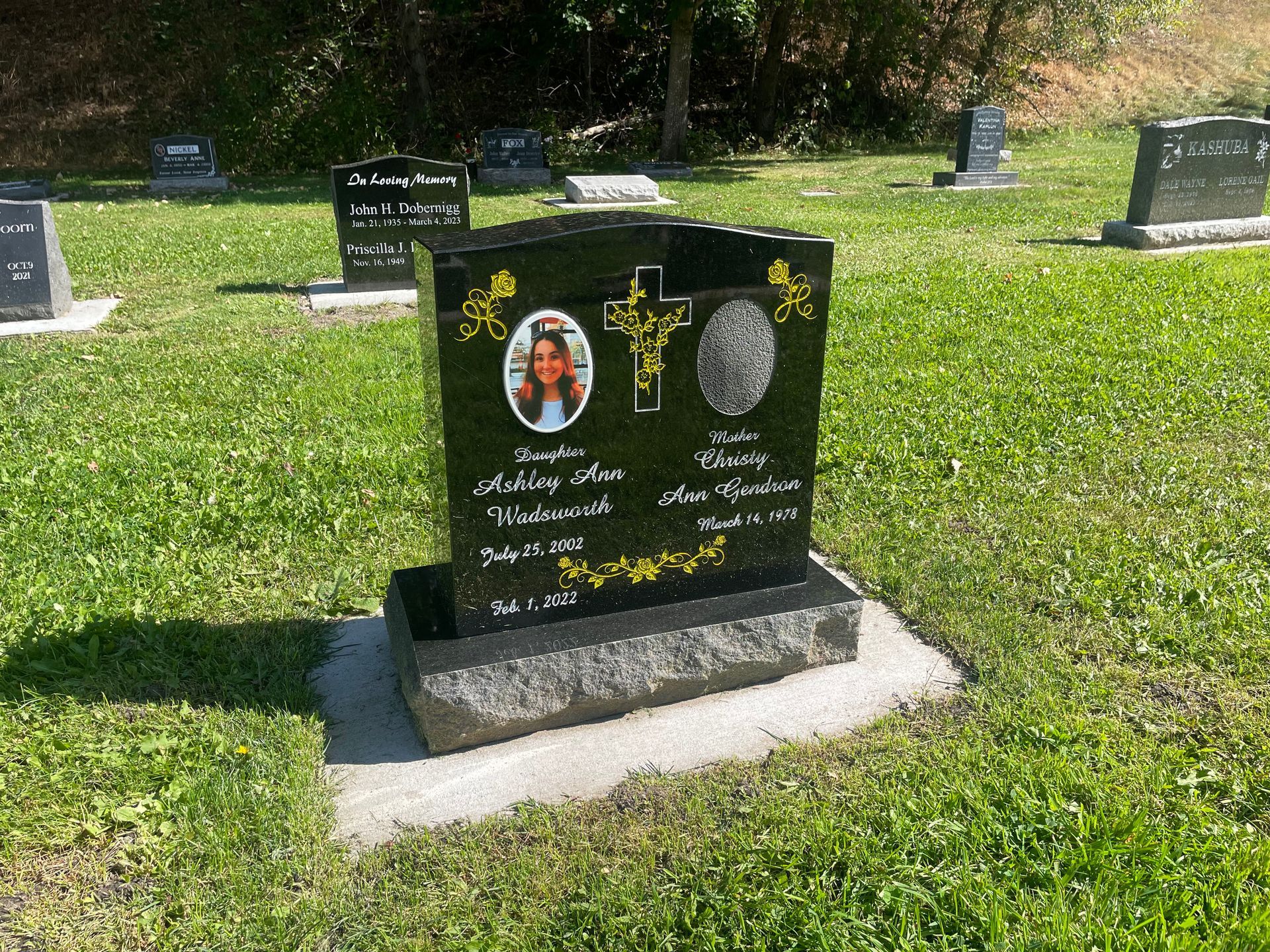 A black gravestone with a picture of a woman on it is in a cemetery.