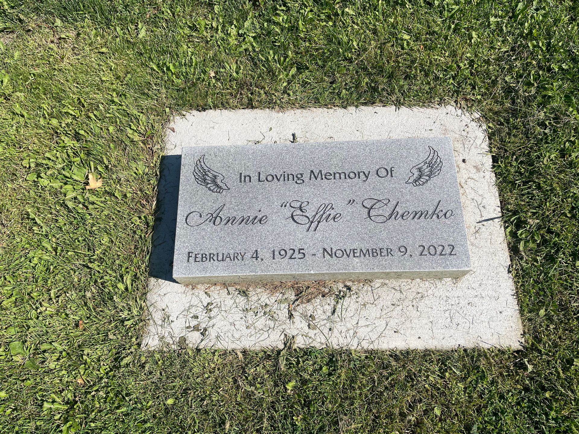 A gravestone for annie effie chomko is sitting in the grass.