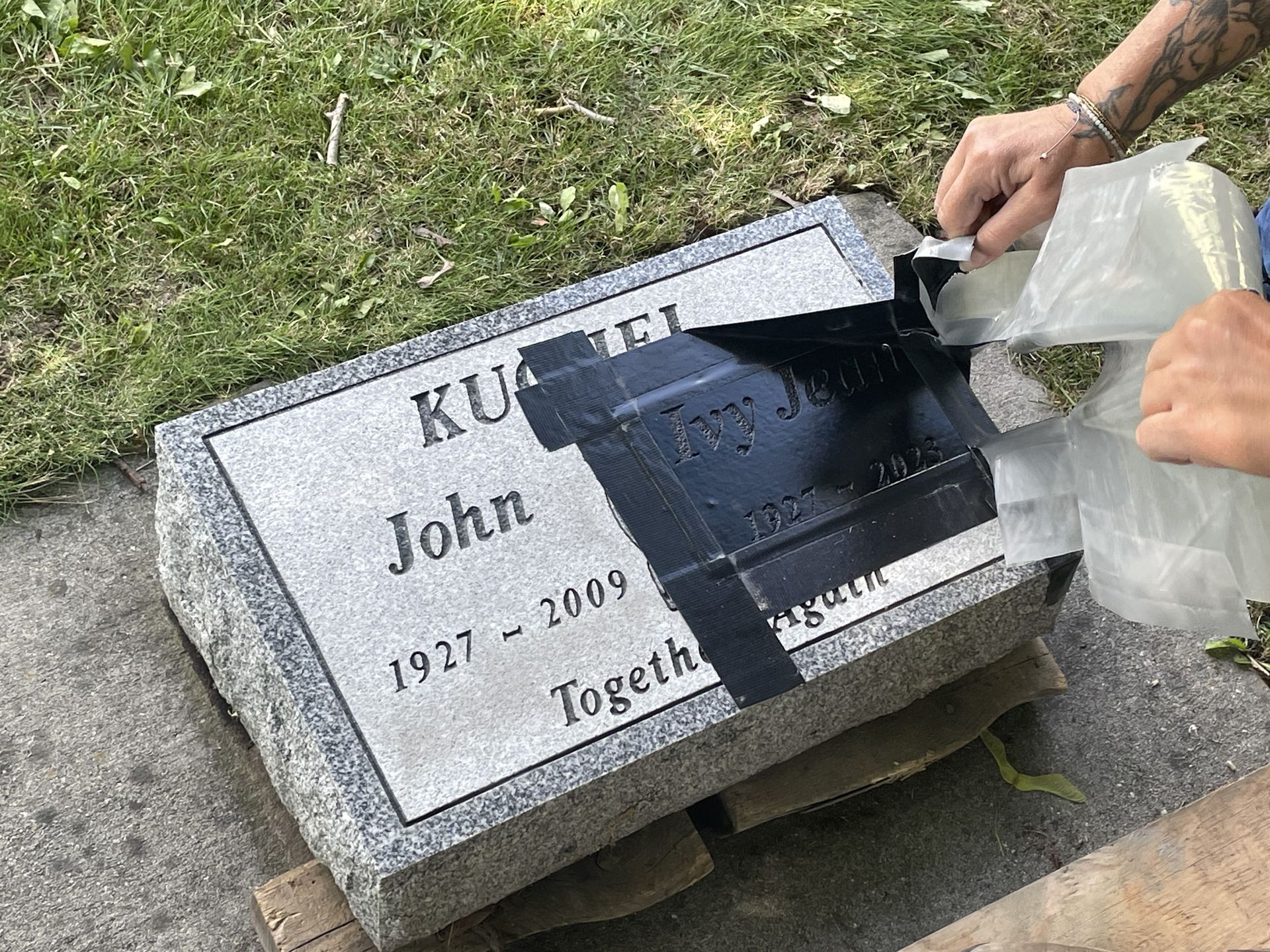 A person is cleaning a gravestone with tape.