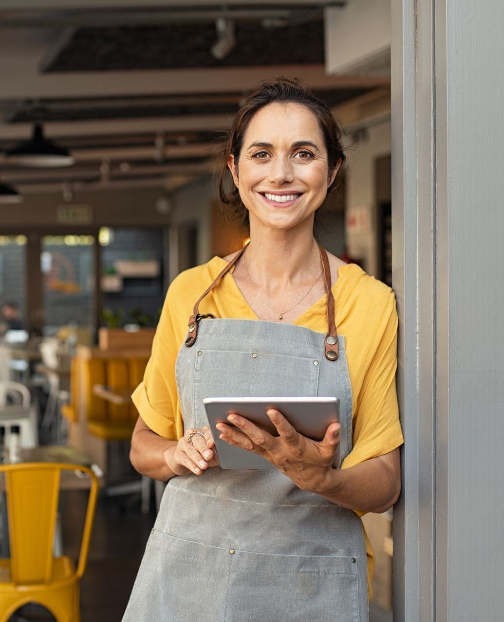 A woman in an apron is holding a tablet in a restaurant.