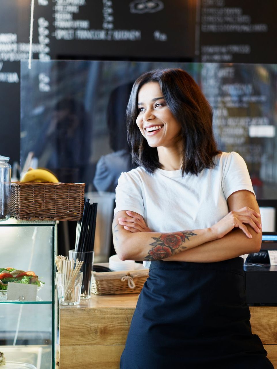 A woman is standing in a restaurant with her arms crossed and smiling.