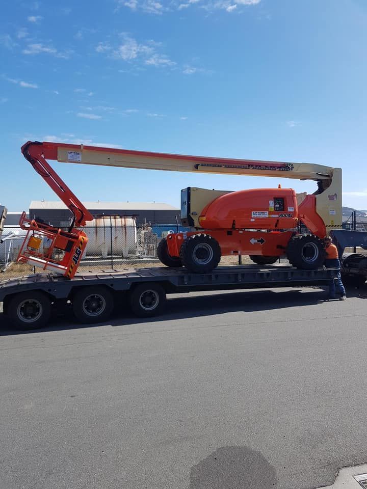 Orange Boom Lift on a Flatbed Trailer in an Industrial Yard Under a Blue Sky — Lifters Hire in Cambridge, TAS