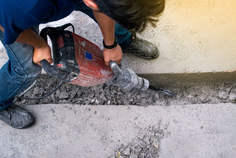 Worker Using a Red Jackhammer to Break Concrete Along a Wall Outdoors — Lifters Hire in Cambridge, TAS