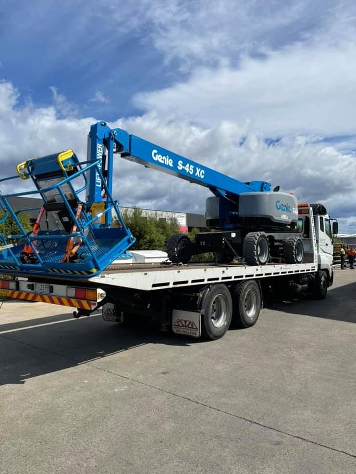 Blue Crane Boom Truck Loading Equipment on a Flatbed Trailer Under a Cloudy Sky — Lifters Hire in Cambridge, TAS