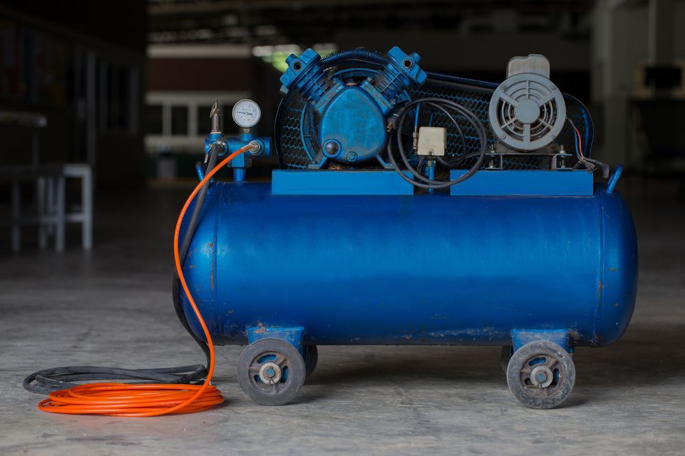 Blue Air Compressor With Orange Hose on a Concrete Floor in a Garage or Workshop — Lifters Hire in Cambridge, TAS