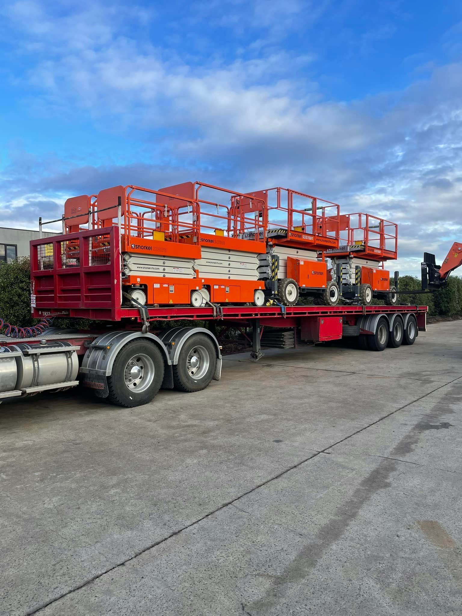 Orange Scissor Lifts Secured on a Red Flatbed Trailer Under a Blue Sky — Lifters Hire in Cambridge, TAS