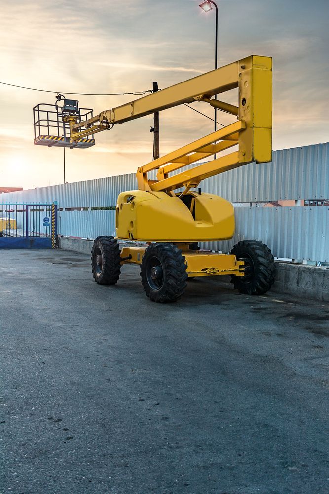 Yellow Boom Lift Parked on Gravel Beside a Metal Fence at Sunset — Lifters Hire in Cambridge, TAS