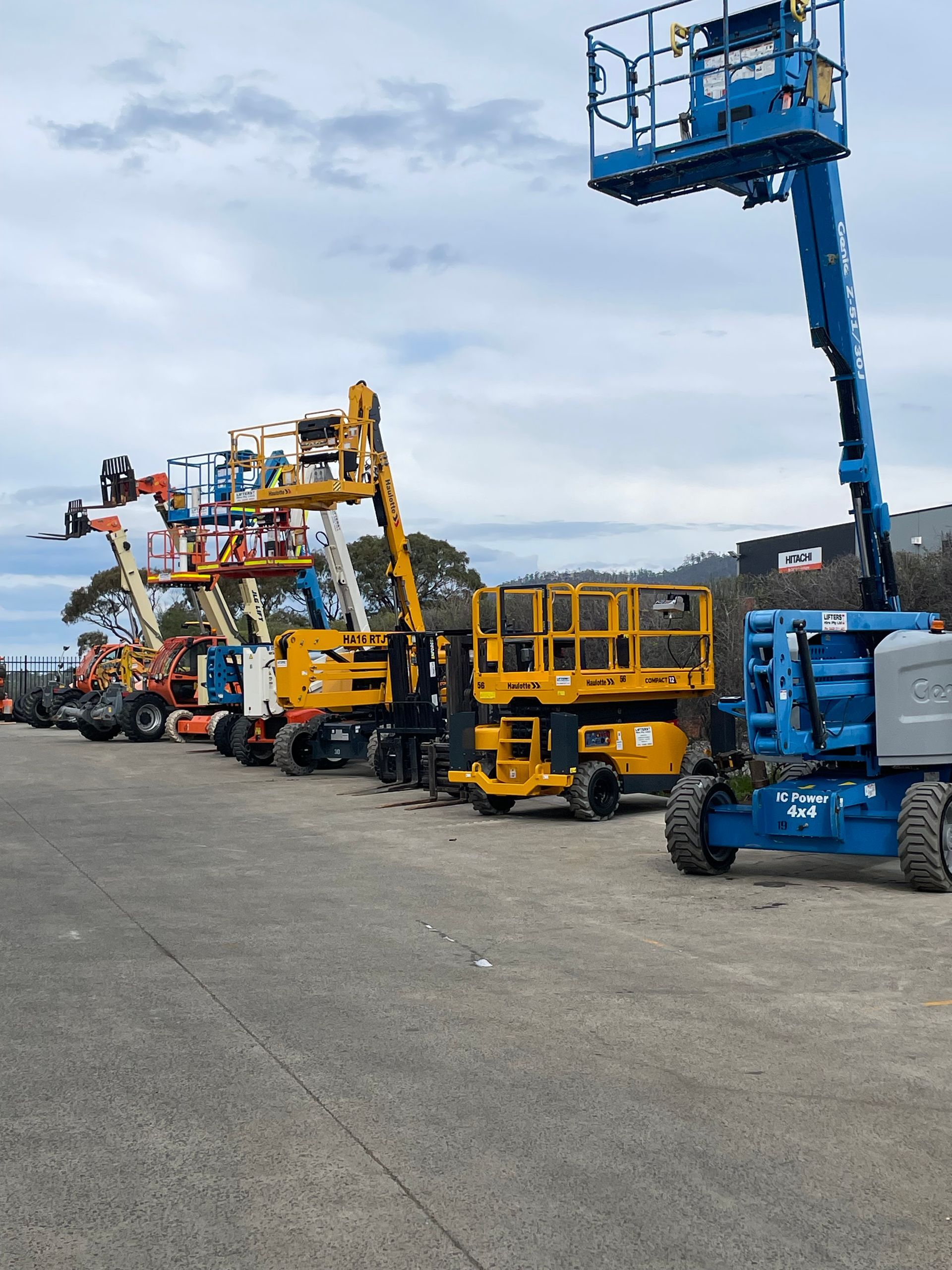 LINE of Colorful Construction Boom Lifts Parked on a Gravel Lot — Lifters Hire in Cambridge, TAS