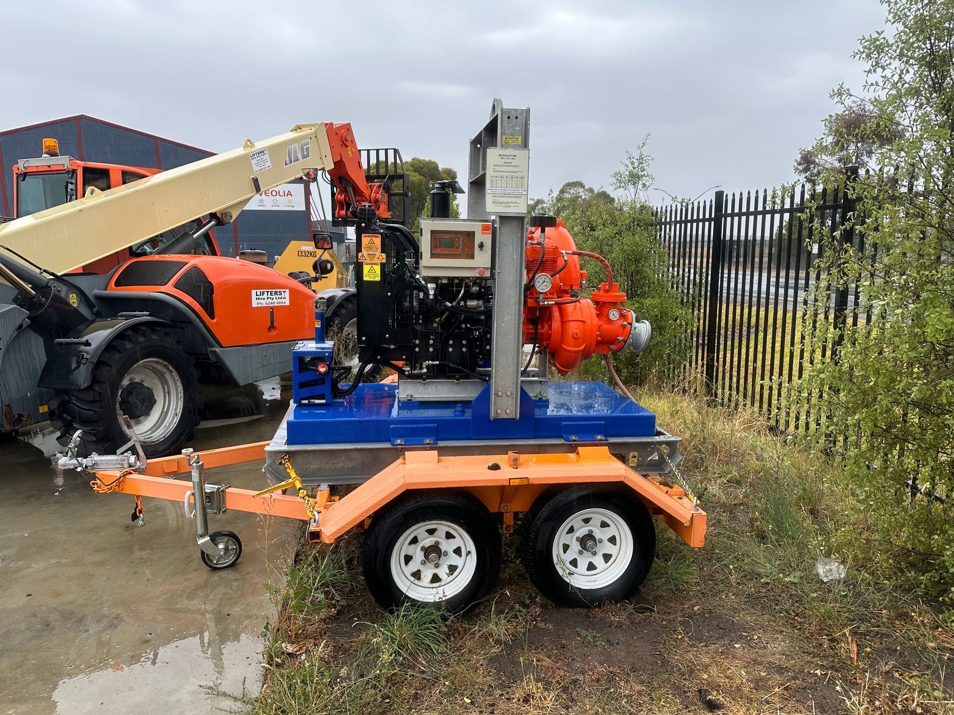 Orange Machinery on a Blue Trailer in a Wet Industrial Yard — Lifters Hire in Cambridge, TAS
