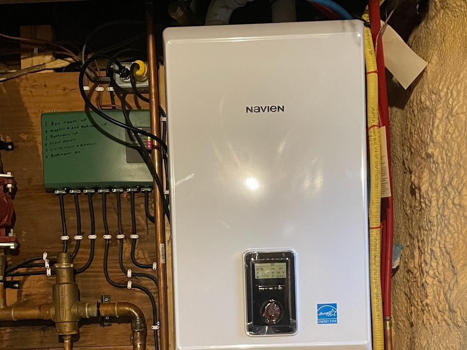 A white boiler is sitting on top of a wooden wall.