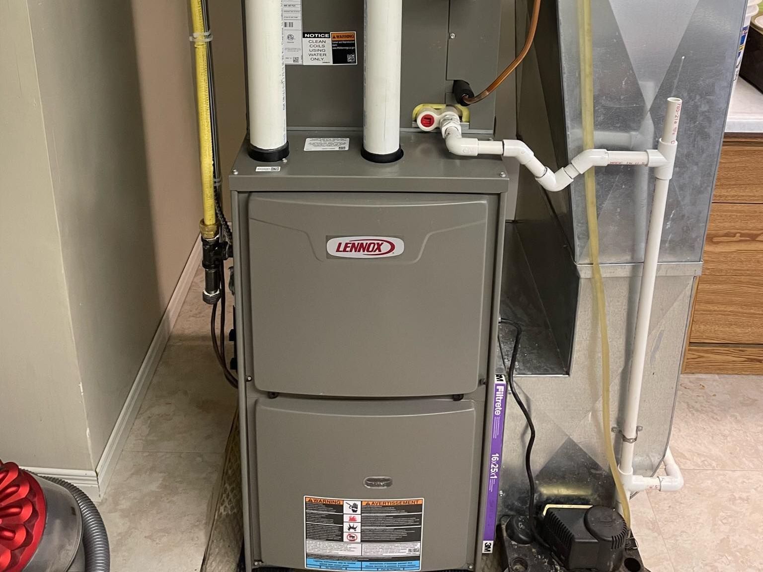 A gray furnace is sitting in a basement next to a wall.