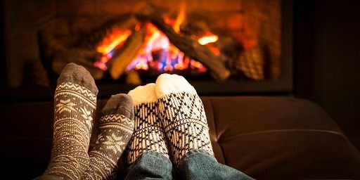 A couple of feet in socks sitting on a couch in front of a fireplace.