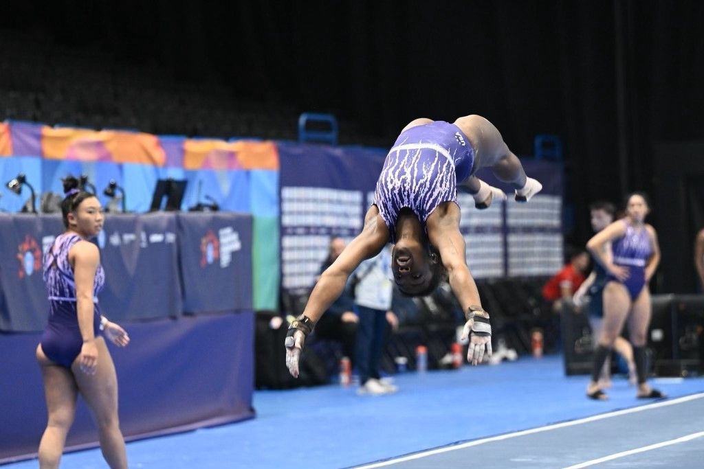 A female gymnast is doing a handstand on a balance beam.