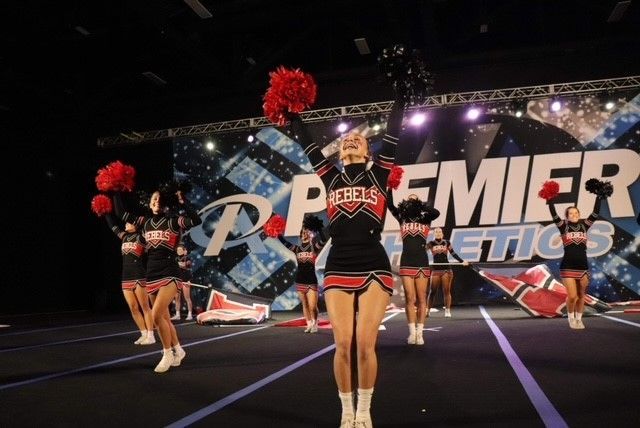 A group of cheerleaders are performing in front of a sign that says premier athletics