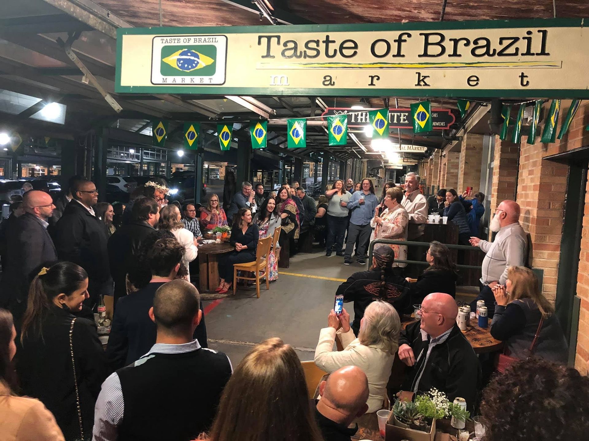 A group of people are gathered under a sign that says taste of brazil