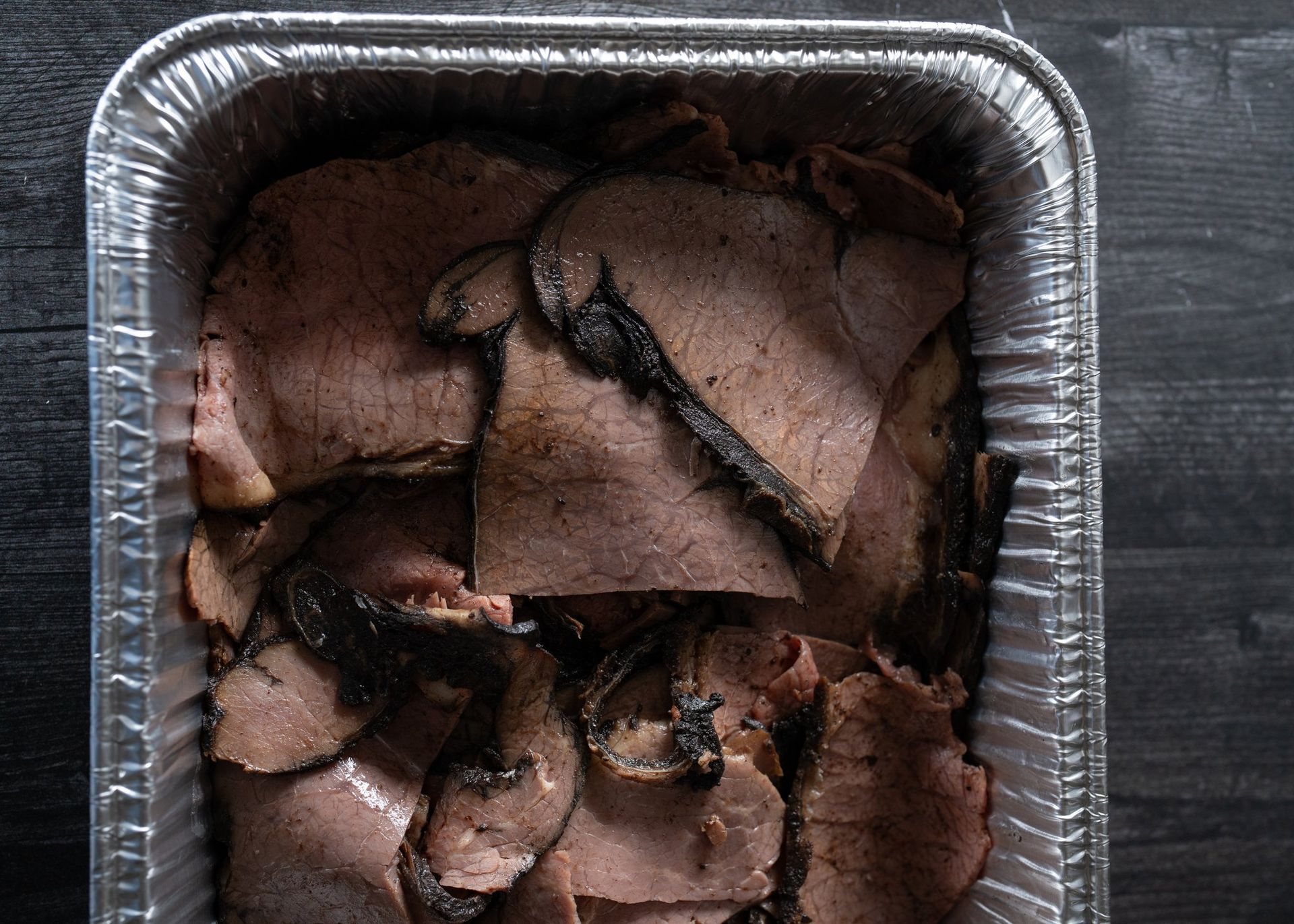 Aluminum foil container filled with sliced meat on a wooden table.