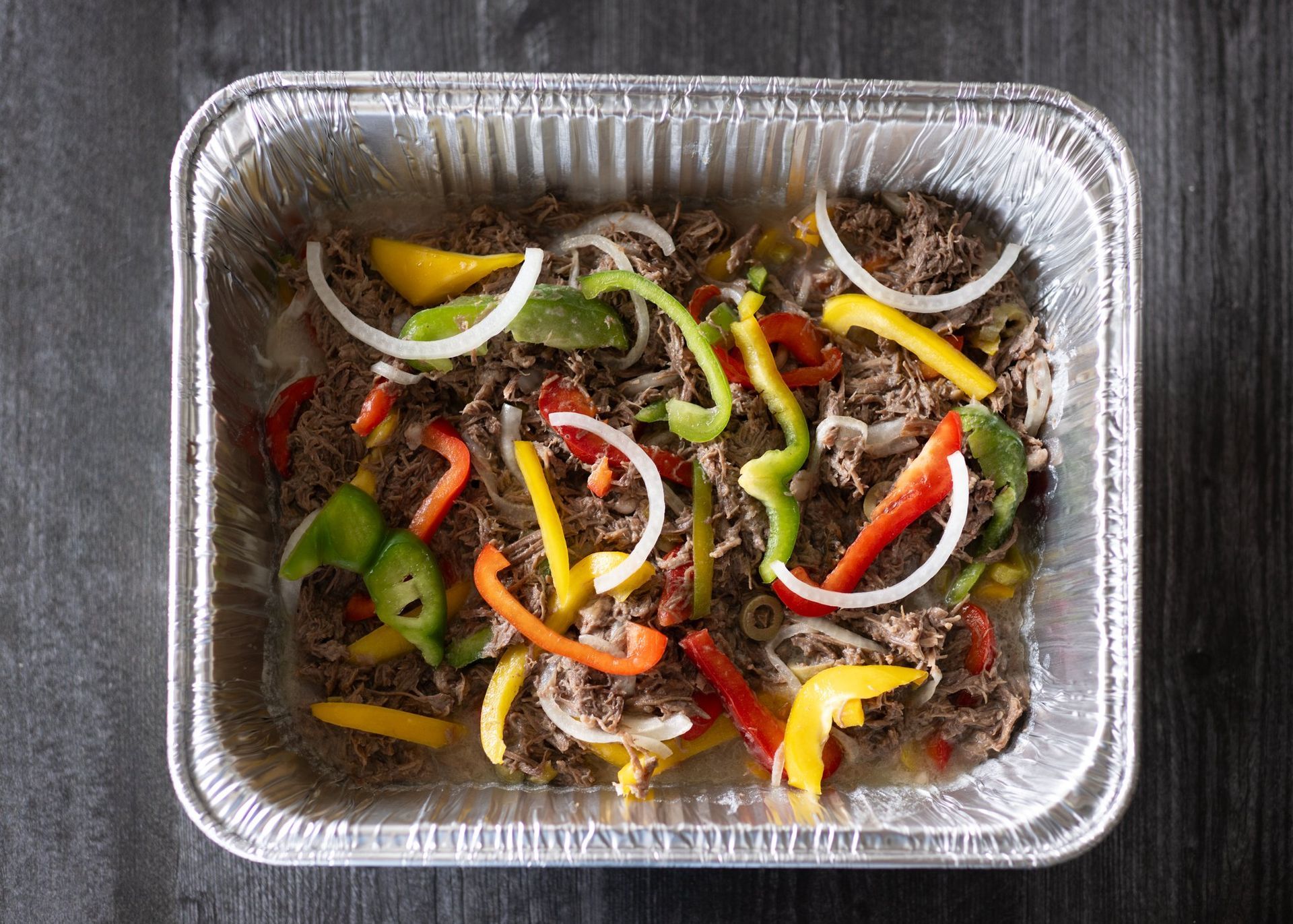 Aluminum foil pan filled with meat and vegetables on a table.