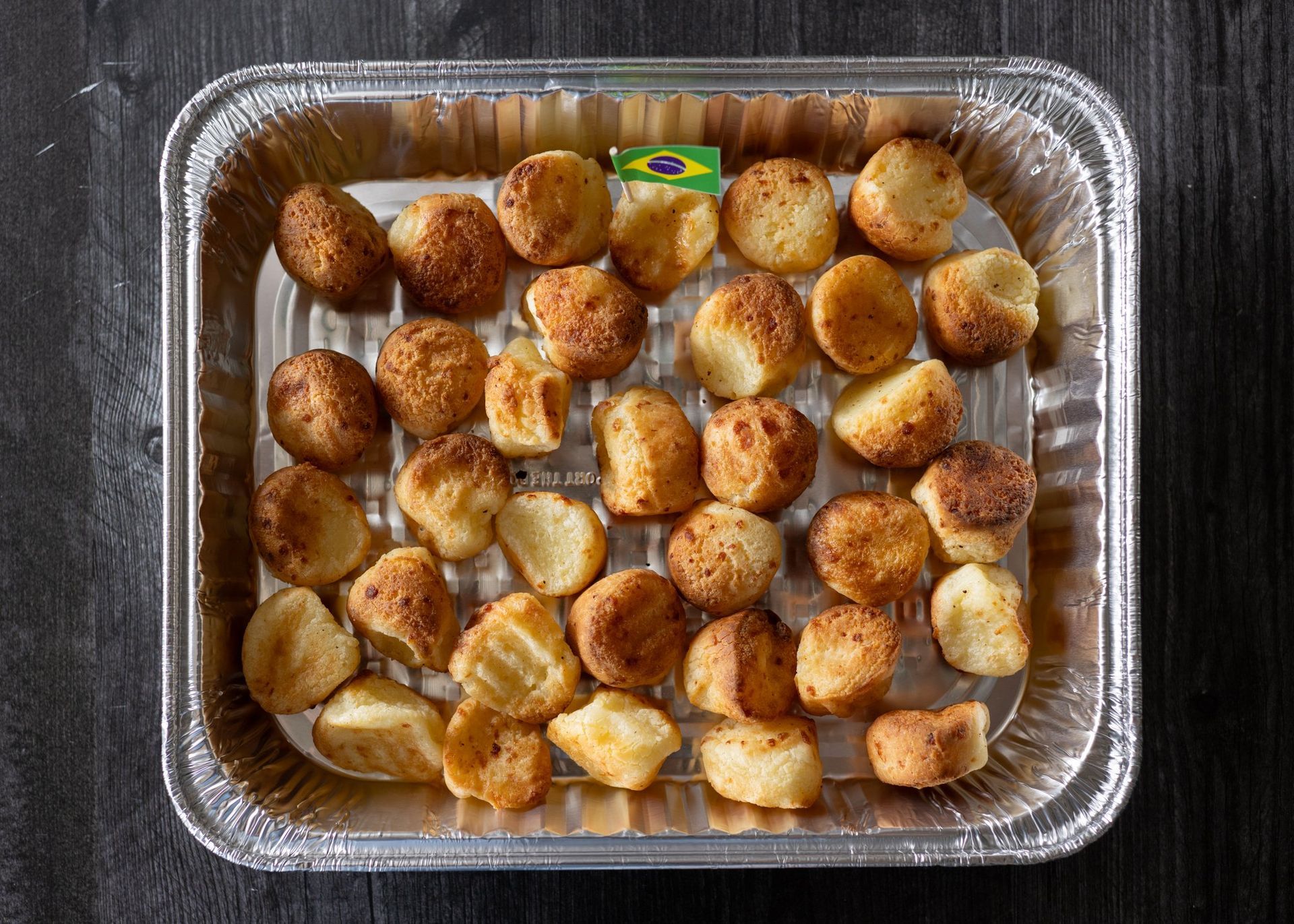 Aluminum foil tray filled with fried potatoes on a grill.