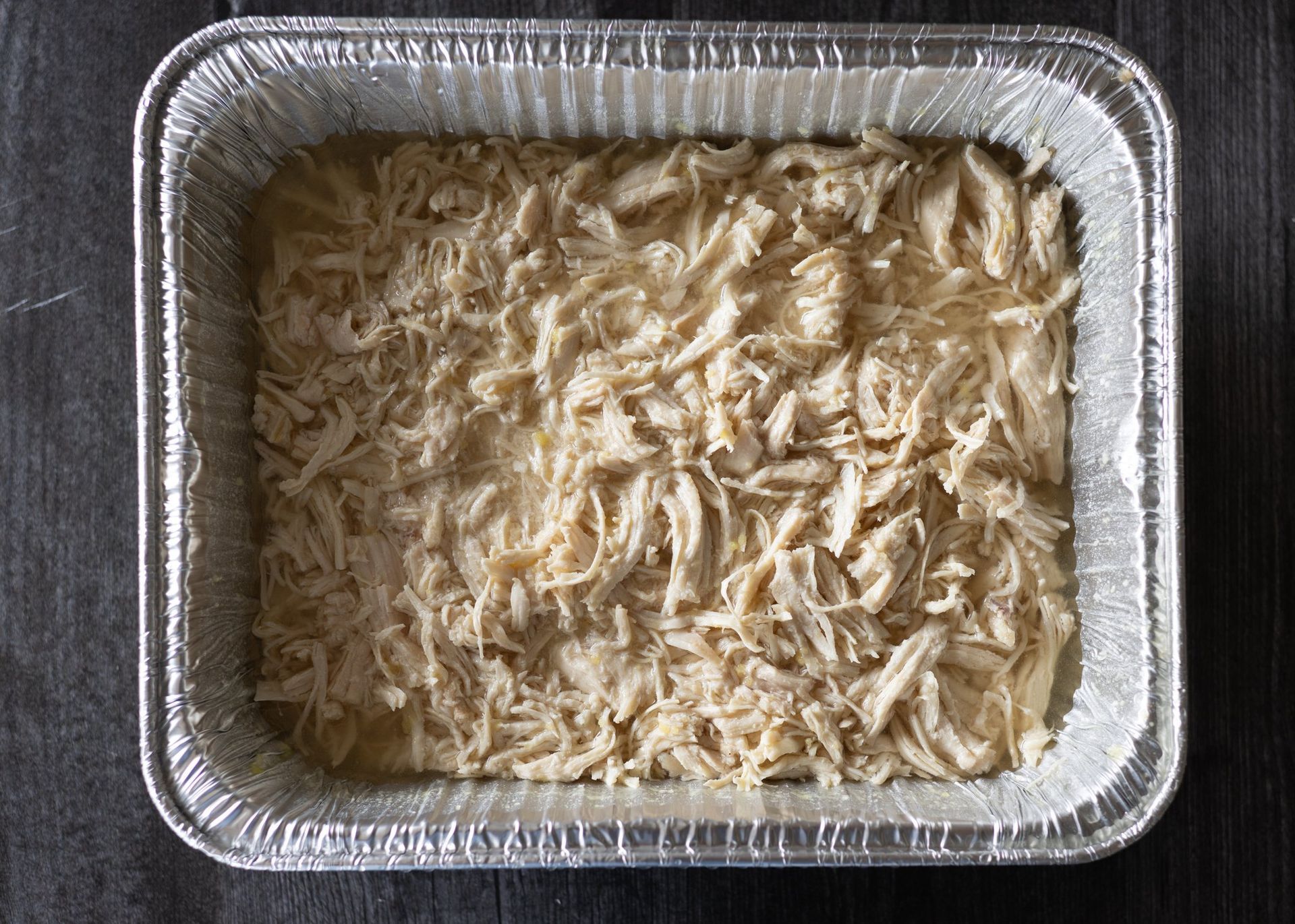 A tin foil pan filled with shredded chicken on a table.