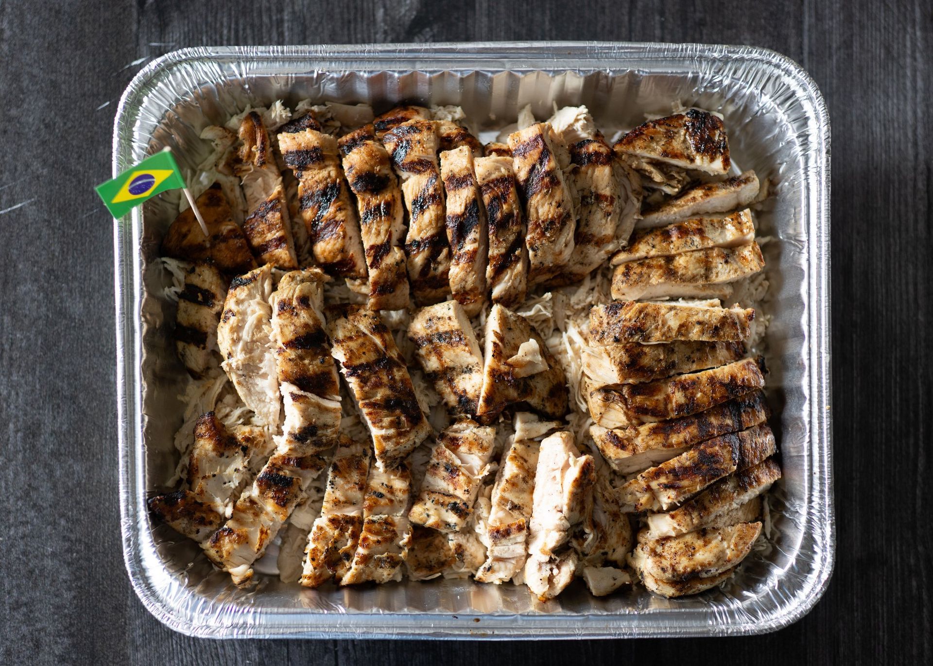A tray of grilled chicken with a brazilian flag sticking out of it.