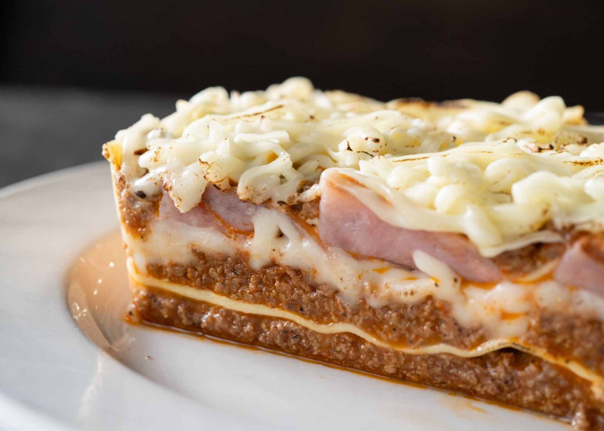 A slice of lasagna with meat and cheese on a white plate.