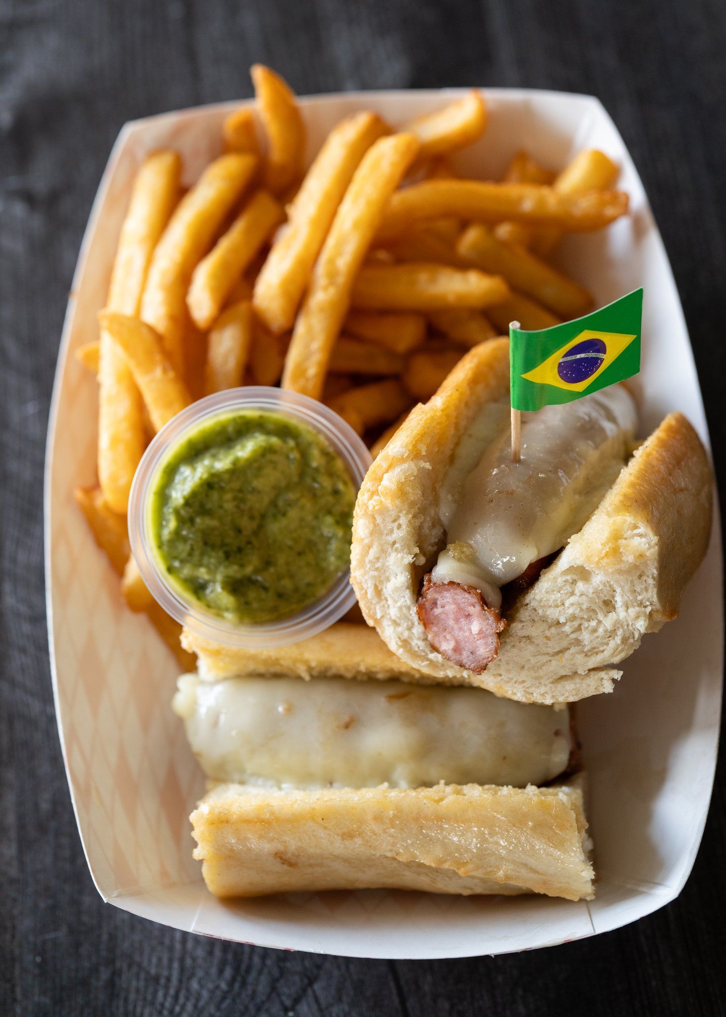 A paper container filled with french fries and a sausage sandwich.