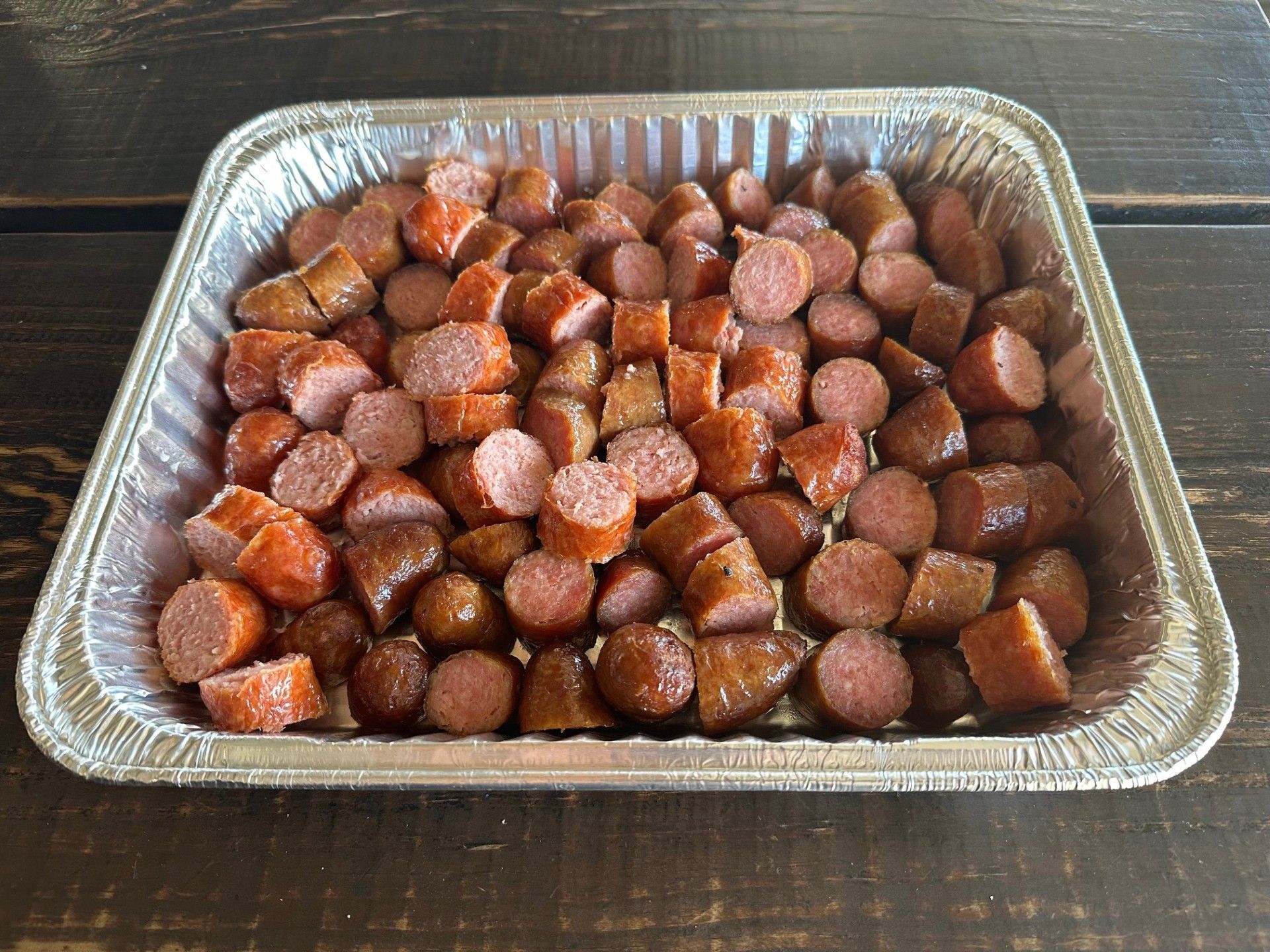 Aluminum foil tray filled with chopped sausages on a wooden table.