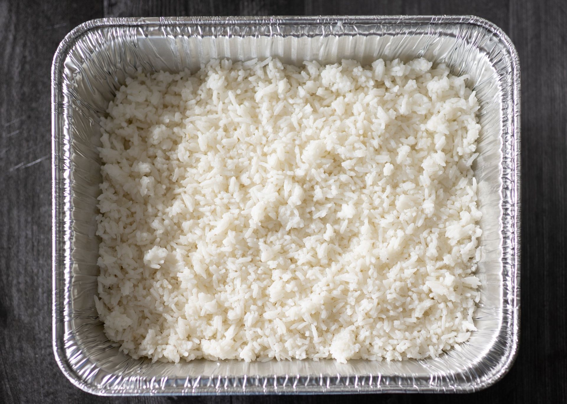 A tin foil pan filled with white rice on a wooden table.