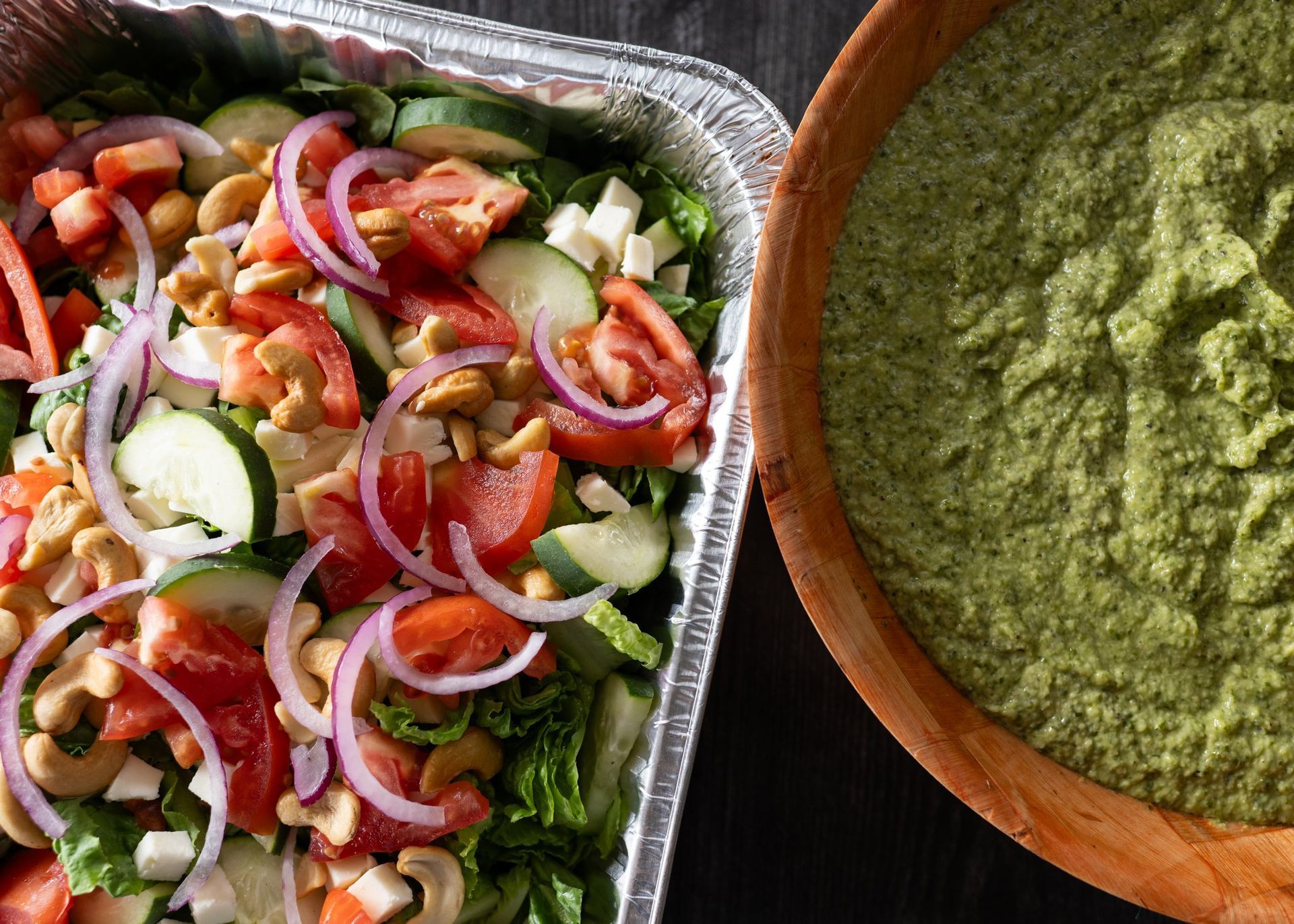 A salad in a tin foil container next to a bowl of guacamole