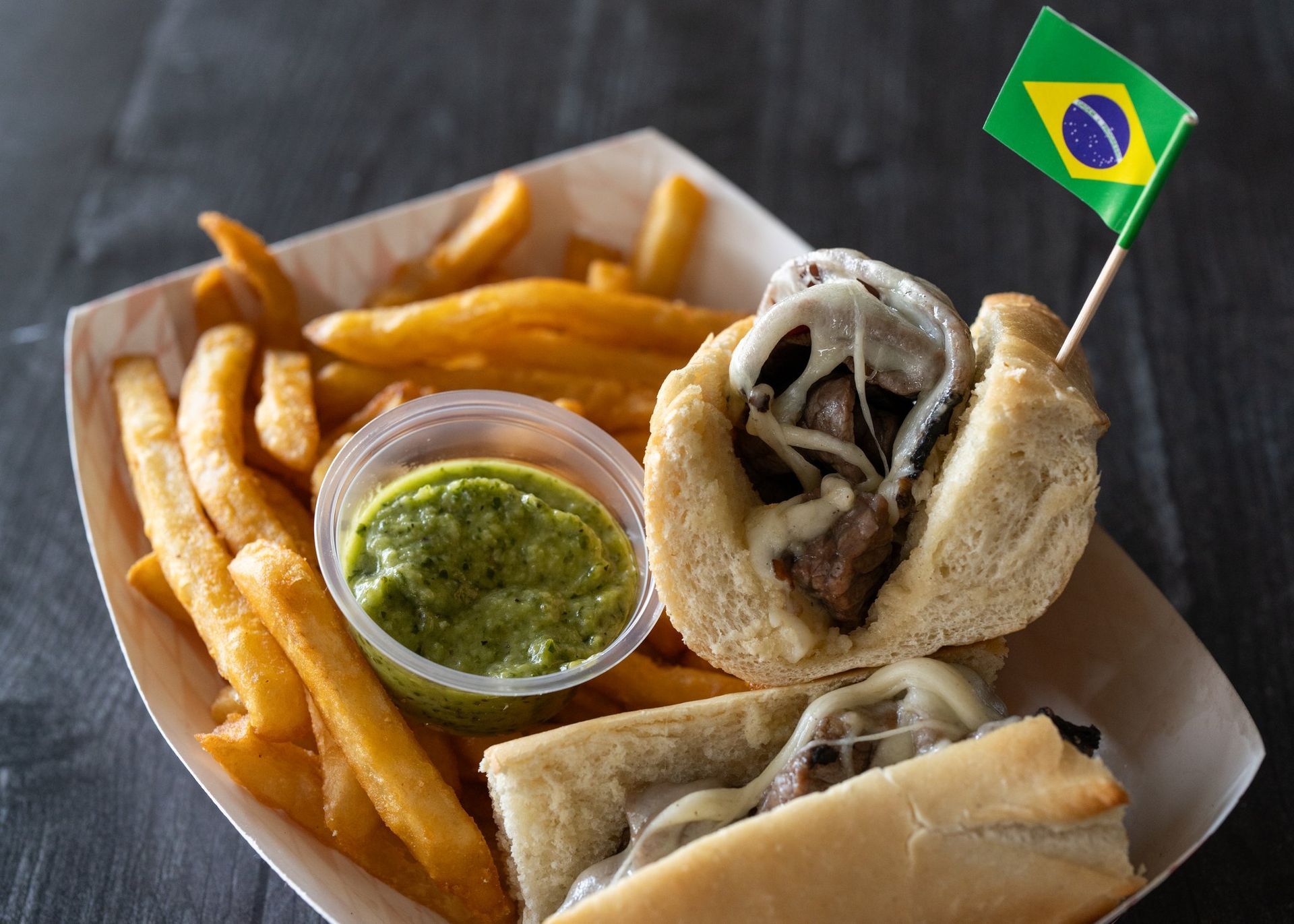 A sandwich with french fries and green sauce on a paper plate.