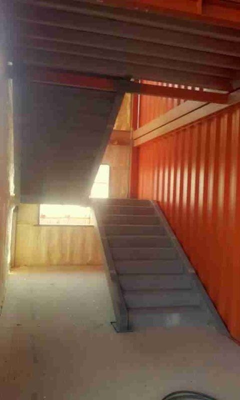 Concrete staircase inside an orange shipping container building under construction, with visible beams and unfinished walls.