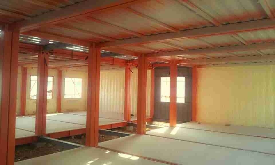 Interior of an orange-painted building framework. Shows support beams, ceiling, windows, and a doorway.