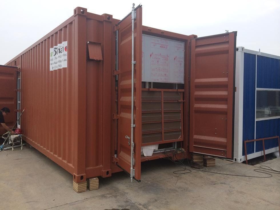 Brown shipping container with open doors, revealing an interior structure. Adjacent to a blue container.