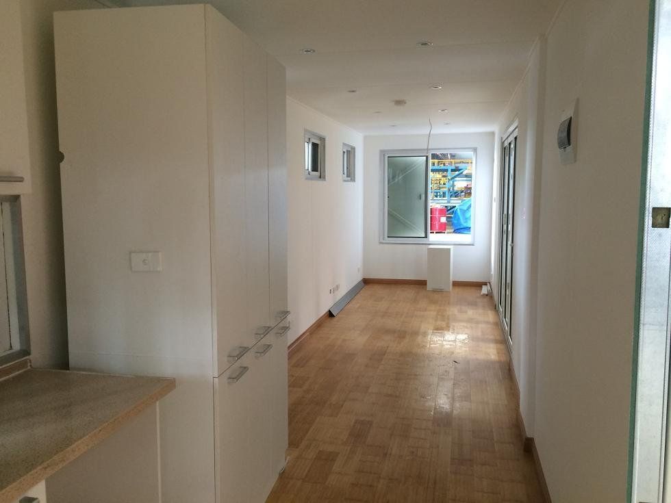 Narrow, white hallway with a long white cabinet on the left and a window at the end, wooden floor.