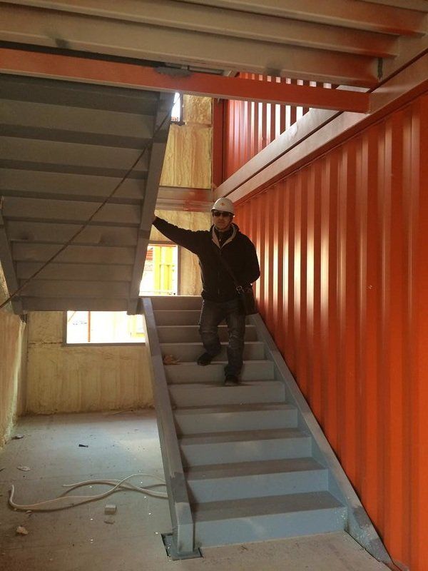 Person in a hard hat walks down stairs inside a building with orange walls and exposed structural beams.