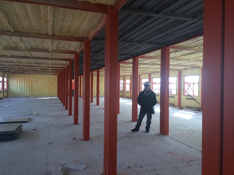 Interior of unfinished building with red support beams; a person stands inside.