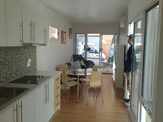 Modern apartment interior with kitchen, dining area, and sliding doors leading to a balcony. A person looks outside.