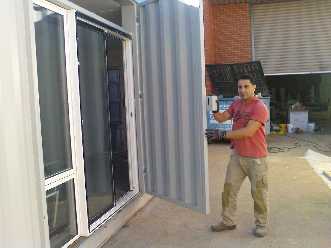 Man holding a large, corrugated metal door next to a building with windows.