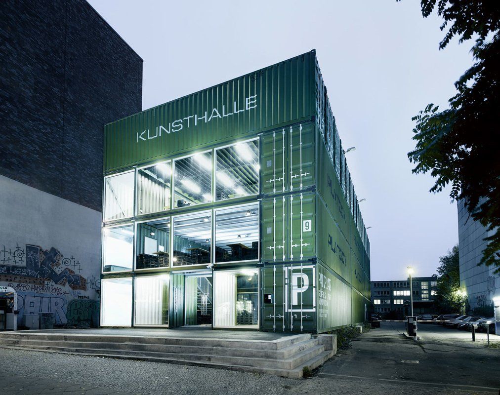 Green Kunsthalle building made of shipping containers; illuminated interior; parking sign.